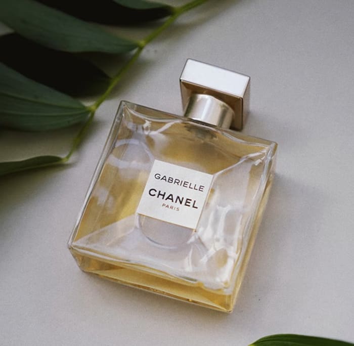 A glass bottle of Parfum lying next to green leaves